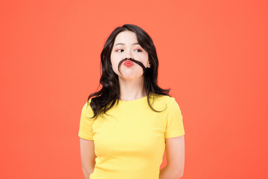 Playful Young Woman with Fake Mustache on Orange Background