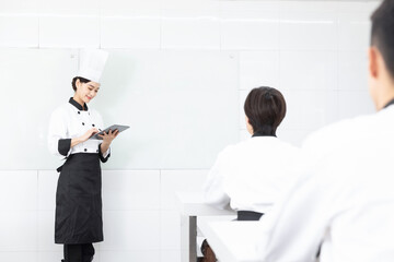 Fototapeta premium Female Chef Instructor Using Tablet During Culinary Class in Professional Kitchen