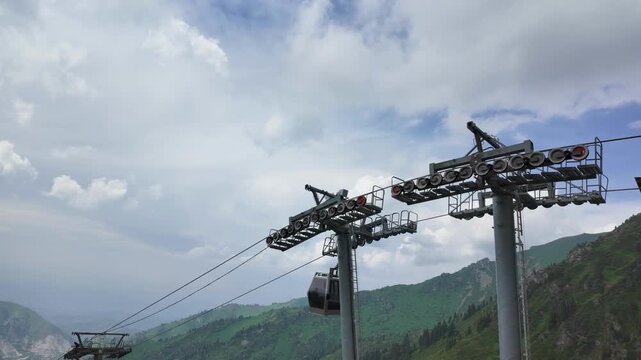 Cable car gondolas moving along steel towers with mountain peaks and cloudy sky in background, Almaty, Kazakhstan