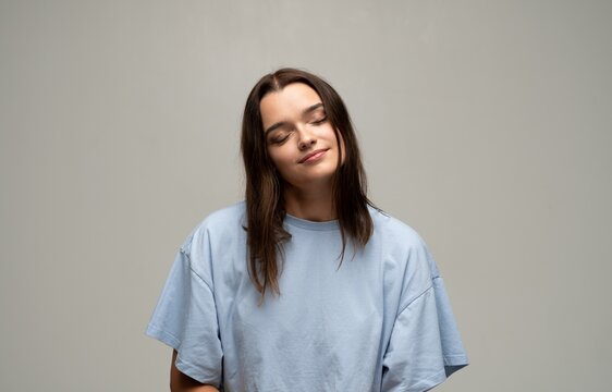 Young woman with eyes closed and a gentle smile, radiating calm, contentment and mindful relaxation in a soft studio portrait