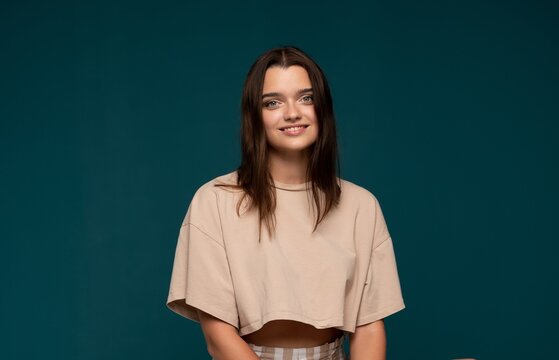 Young smiling woman posing confidently, expressing happiness, youth, and positive emotions against a blue background