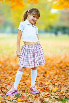 Autumn girl wears a sequin jacket. Autumn child carries maple leaves. Colorful autumn foliage blurs behind. Happy autumn lifestyle portrait.