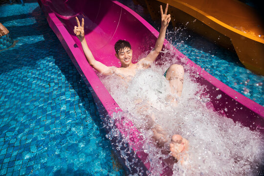 Young man splashing down water slide at summer water park