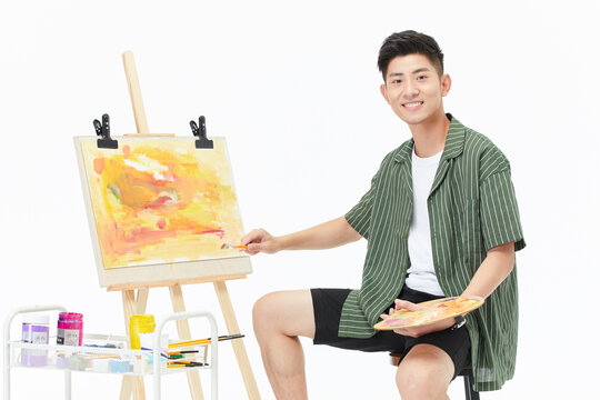 Smiling young male painter working on abstract canvas at easel in bright studio