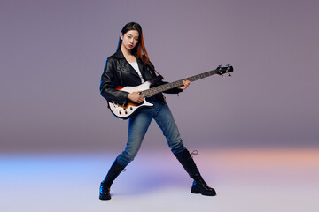 Fototapeta premium Young woman playing bass guitar in confident rock pose