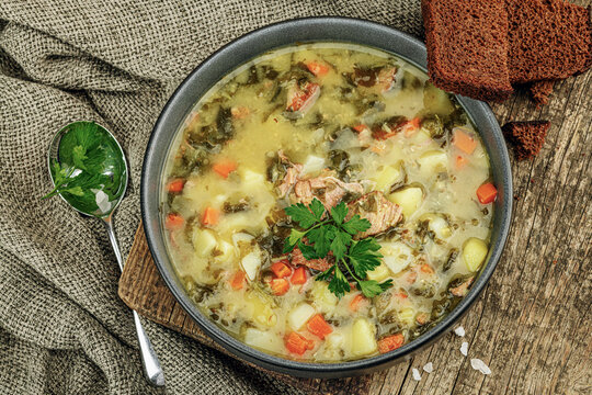 Traditional green sorrel soup with meat, eggs and vegetables in a black ceramic bowl. Rye bread
