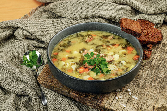 Traditional green sorrel soup with meat, eggs and vegetables in a black ceramic bowl. Rye bread