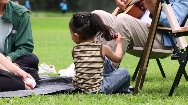 Asian kids painting in park. Asian family enjoy outdoor picnic with food and drinks in park sunny day, outdoor activitie with daughter father, mother grandfather. GrandFather playing acoustic guitar