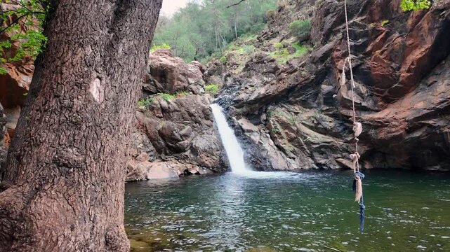 Toparlar waterfall cascading into crystal clear natural swimming pool surrounded by rocky cliffs with rope swing, Mugla, Turkey