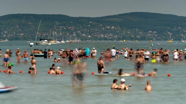 Lake Balaton cross-swim event timelapse with moving crowd of swimmers across water towards green hills shore under bright summer sun