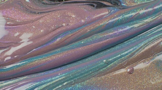 Pearlized pigment creating shifting opalescent waves in a colorful liquid mixture with shimmering metallic swirls.