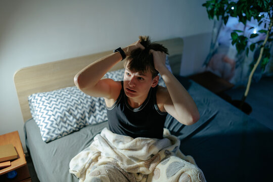 High angle of a stressed teenage boy pulling his hair in the dark bedroom.