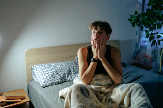 Side view of an anxious teenage boy having a panic attack in bed.