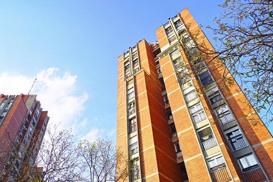Low angle view of brick high-rise apartment tower pointing toward blue sky in Vidikovac, Belgrade. Captures graphic urban geometry, vertical real estate growth, and late modernist aesthetics.
