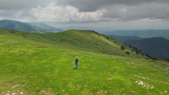 Person Standing in Sunlit Pyrenean Mountain Meadow Under Dramatic Clouds