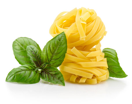 Uncooked tagliatelle pasta nests with fresh aromatic basil leafes for cooking isolated on white background