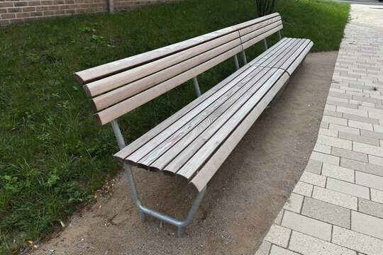 A long wooden bench in a park near a walking path