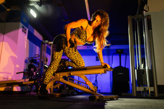 Woman exercises with weights in a gym during evening hours while using a weight bench for strength training