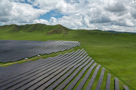 High-Angle Aerial View of Solar PV Panel Array on Zoige Grassland Mountains, Aba, Sichuan: Renewable Clean Energy, Agrivoltaics, Green Hills, Blue Sky and Cloud Background