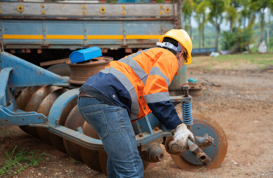 Agricultural mechanic maintains a disc harrow on heavy farm machinery, wearing safety gear while inspecting mechanical components for reliable operation, preventive service, and field productivity.