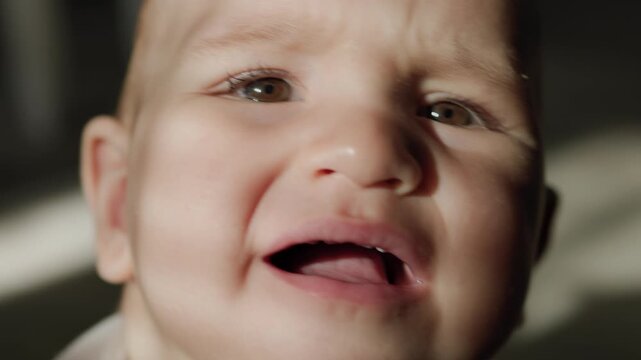 Infant in the teething phase crawling on an indoor floor and biting a silicone teether. Strong sunlight casts distinct shadows across the baby's face and body during daytime.