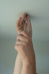 A man's hands use a screwdriver to attach a section of ceiling cornice, performing home renovation work overhead. © Ann