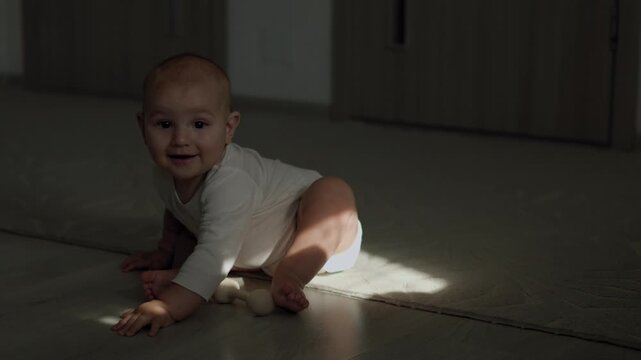 Infant in the teething phase crawling on an indoor floor and biting a silicone teether. Strong sunlight casts distinct shadows across the baby's face and body during daytime.