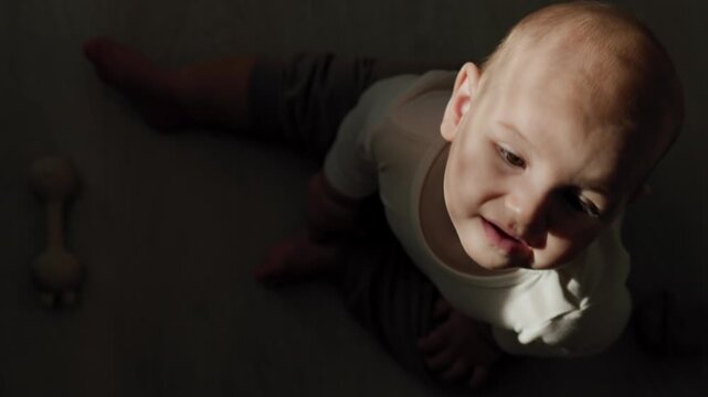 Infant in the teething phase crawling on an indoor floor and biting a silicone teether. Strong sunlight casts distinct shadows across the baby's face and body during daytime.