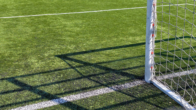Football goal net and dramatic shadow on artificial turf, representing competition, sports marketing, teamwork, achievement and game day readiness concept