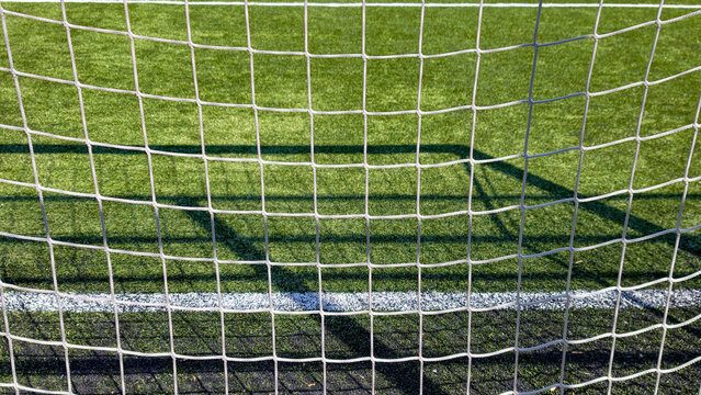 Soccer goal net framing a vibrant green artificial turf field with white line, symbolizing achieving success, sports aspirations, and clear targets