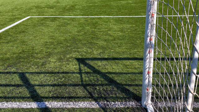 Soccer goal shadow crossing artificial turf field with white line, symbolizing sports ambition, achievement, and competition in modern athletic environment