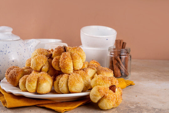 Pumpkin spice buns with almond nuts, cinnamon and sugar crunch. Autumn baking idea, pumpkin puree based vegetable rolls in form of small pumpkins. Tiny sweet pumpkin shaped buns on white plate,