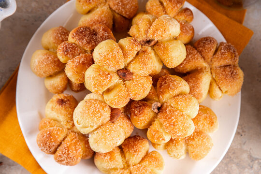 Pumpkin spice buns with almond nuts, cinnamon and sugar crunch. Autumn baking idea, pumpkin puree based vegetable rolls in form of small pumpkins. Tiny sweet pumpkin shaped buns on white plate,