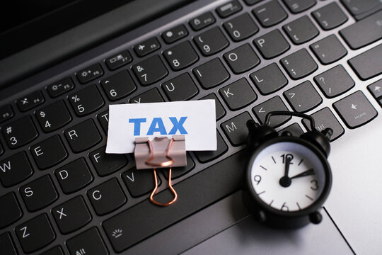 A paper with the word "tax" written on it, a paperclip, and an alarm clock on a keyboard.