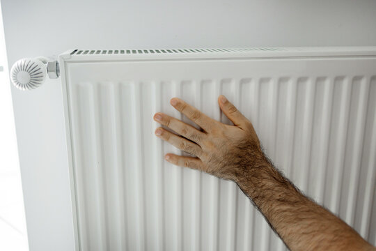 Hands adjusting a white radiator thermostat and feeling the heater. The set includes 50 Euro banknotes and a black wallet placed on the heating equipment.