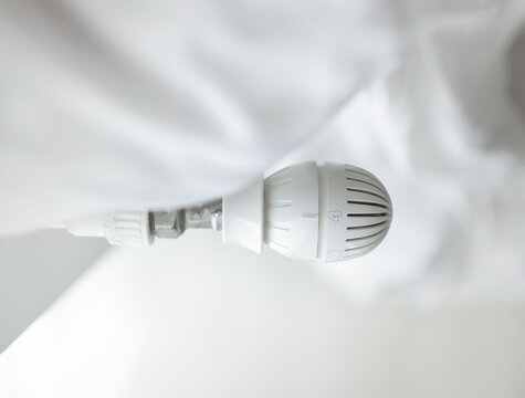 Hands adjusting a white radiator thermostat and feeling the heater. The set includes 50 Euro banknotes and a black wallet placed on the heating equipment.
