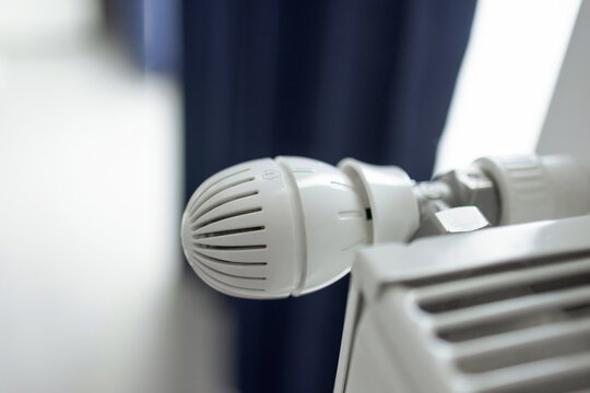Hands adjusting a white radiator thermostat and feeling the heater. The set includes 50 Euro banknotes and a black wallet placed on the heating equipment.