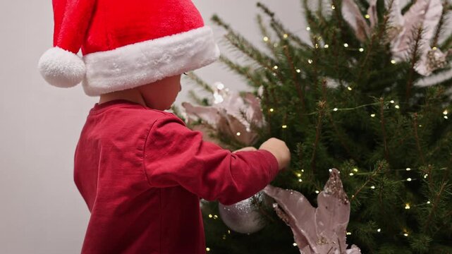 Close-up shots of two boys and their grandmother decorating a Christmas tree indoors. The brothers wear festive hats and pet a black cat near winter ornaments and a toy snowman.