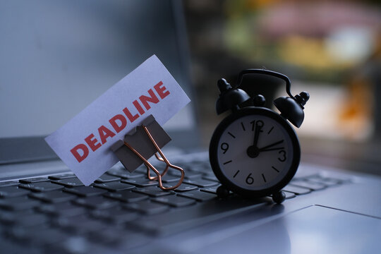 "Deadline" text and a small alarm clock on a laptop keyboard. Deadline and work concept with text on an alarm clock on a desk. Motivation and management. Racing against time. Working under pressure.