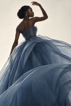 Elegant woman in strapless light-blue tulle ball gown posing gracefully outdoors with soft natural lighting, ethereal wedding or formal event attire, flowing voluminous skirt, timeless bridal fashion