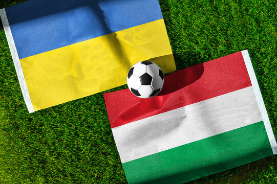 Ukraine vs. Hungary football match. National flags on green grass with soccer ball in the middle. Football background for international match.