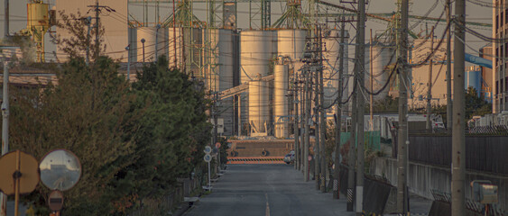 電柱と電線が張り巡らされた臨海工業地帯の道路と工場のサイロ風景 © suisounonou