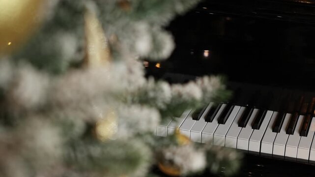 Close-up video shots of a frosted Christmas tree decorated with gold and white baubles. The indoor background features warm string lights bokeh and a black piano keyboard.