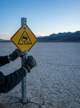 Worker tightening a bolt on a yellow road warning sign in a desert plain
