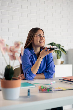 Woman sending voice message using smartphone at office desk