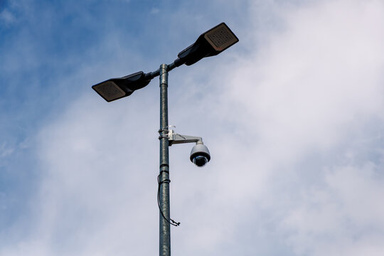Modern dual LED street lights with CCTV dome security camera mounted on metal pole under blue cloudy sky, smart city and public surveillance concept
