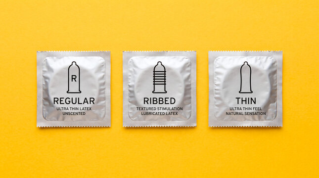 Three silver condom foil packets with different texture labels arranged on a bright yellow background