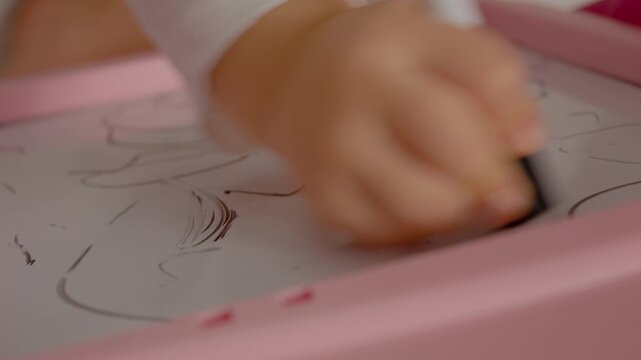 In a cozy room, a child uses chalk to draw on a blackboard. The hands focus on creating and erasing, exploring imagination through art.