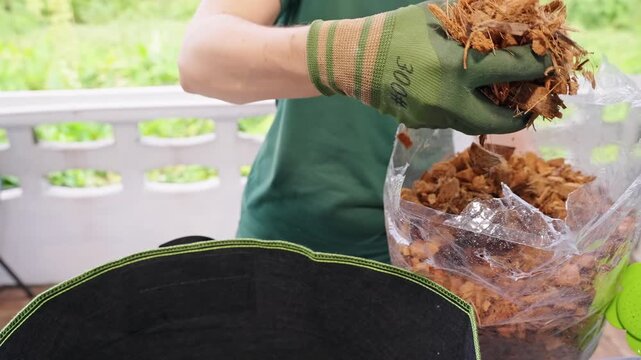 Gloved Person Adds Coconut Husk Mulch to a Fabric Planter on a Balcony, Supporting Container Gardening, Plant Care, and Sustainable Growing