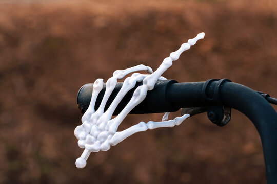 White plastic skeleton hand gripping black rubber handle of vintage bicycle for Halloween outdoor display. Concept for Halloween prop details, creepy cycling themes, dead rider, outdoor haunted setup.